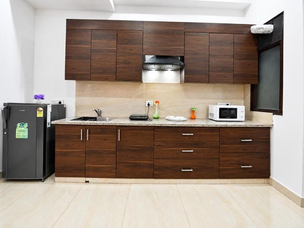 A kitchen with dark wood cabinets, a stainless steel range hood, a microwave, and a refrigerator.