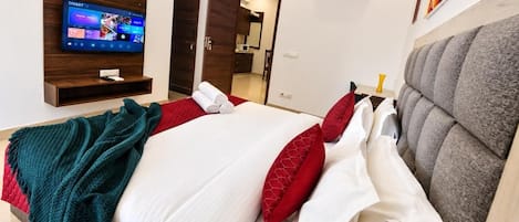 A hotel room with a bed, a TV, a wall-mounted air conditioner, and a door leading to a bathroom.