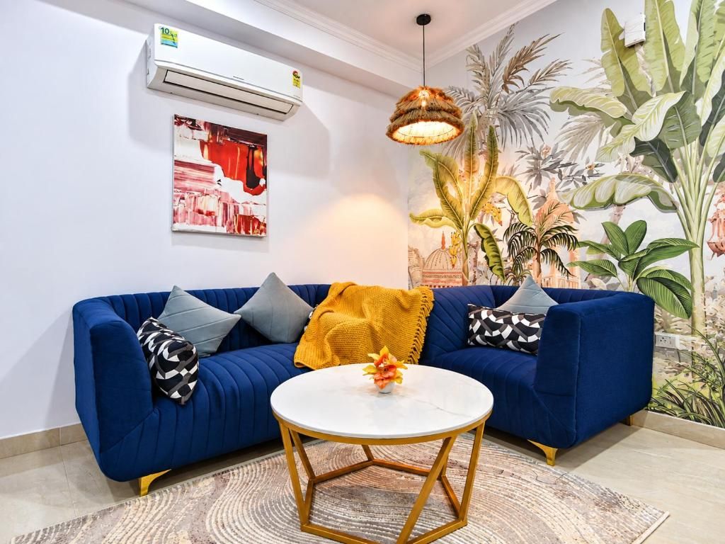 Ein Wohnzimmer mit einem blauen Sofa, einem weißen runden Tisch und einem Wandbild im tropischen Stil.