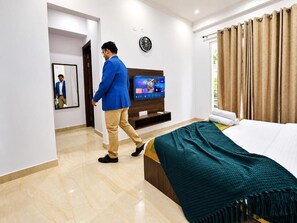 A hotel room with a bed, a TV, a clock, and a mirror. - Daffodil Hotel & Service Apartment-  1 BR apartment 6 (Gurugram)