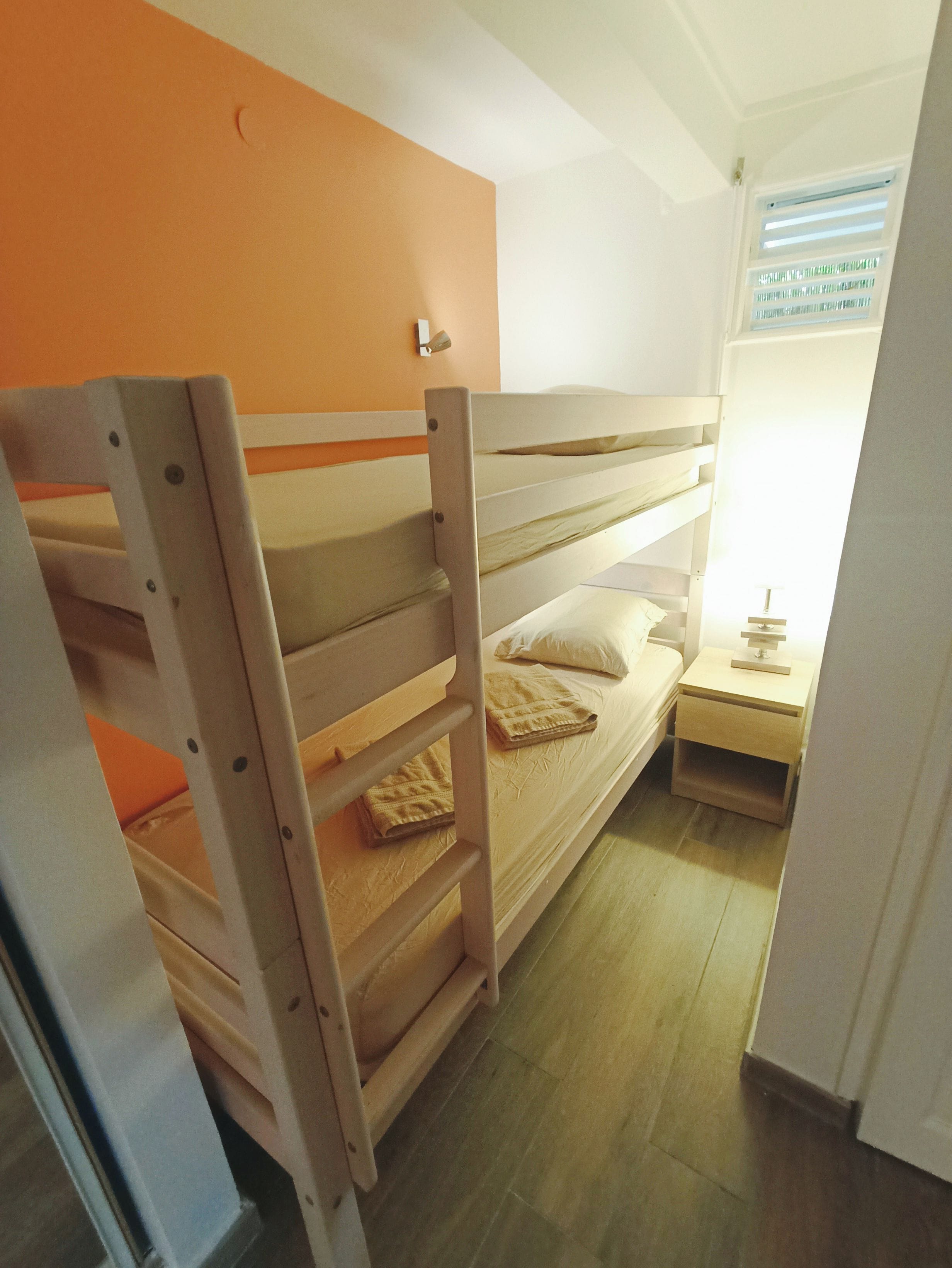A bunk bed with a nightstand and a lamp, a window with blinds, and a door.