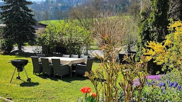 A garden with a barbecue area, outdoor seating, and a variety of plants and flowers.