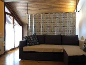Quarto com teto de madeira, sofá com almofada estampada e cortina com desenho paisley.