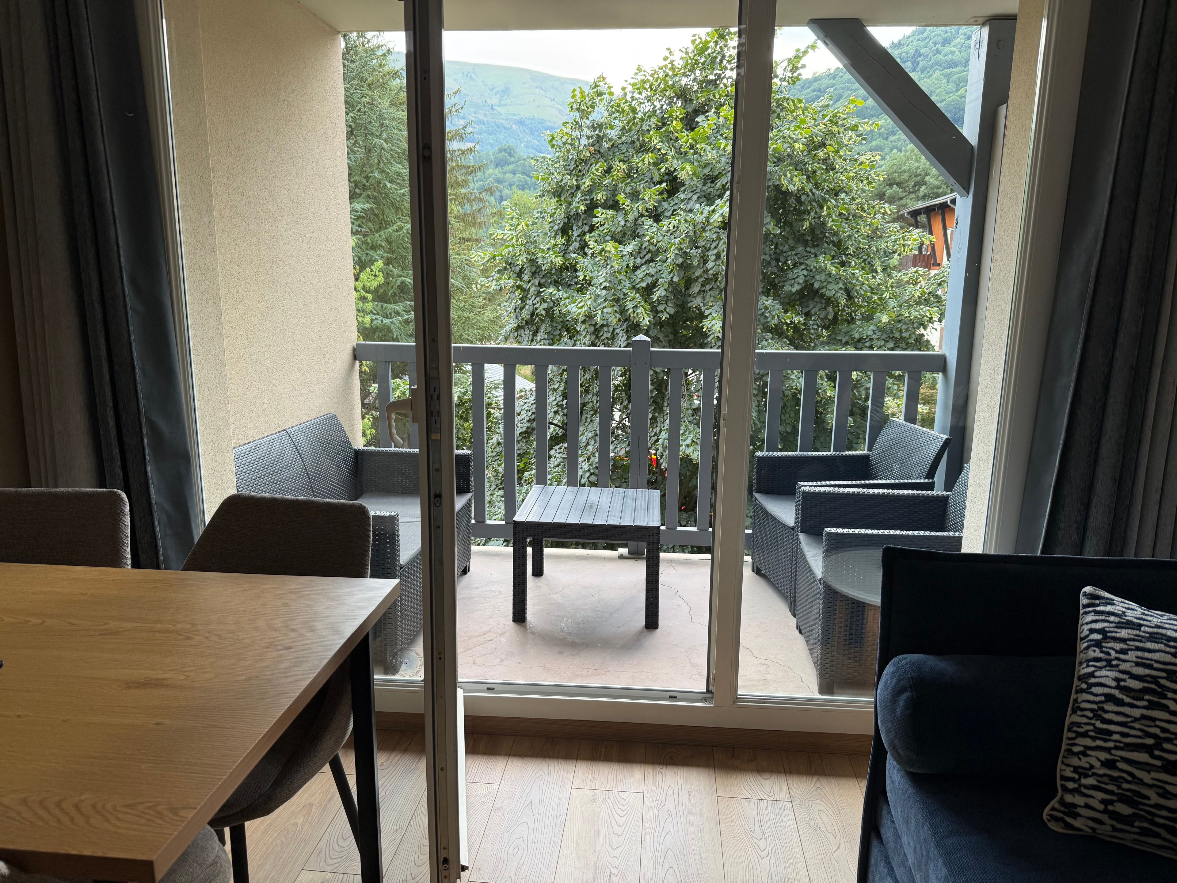Un balcón con mobiliario de mimbre, una mesa de madera y vistas a zonas verdes y colinas.