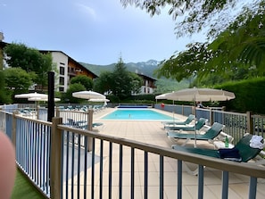 A pool area with lounge chairs and umbrellas, surrounded by greenery and buildings. - Apartment 'Bel Appartement À Saint-lary-soulan' with Mountain View and Shared Pool (Saint-Lary-Soulan)