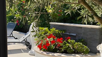 Un jardín con un cantero blanco lleno de flores rojas, una pared de piedra y una silla blanca.