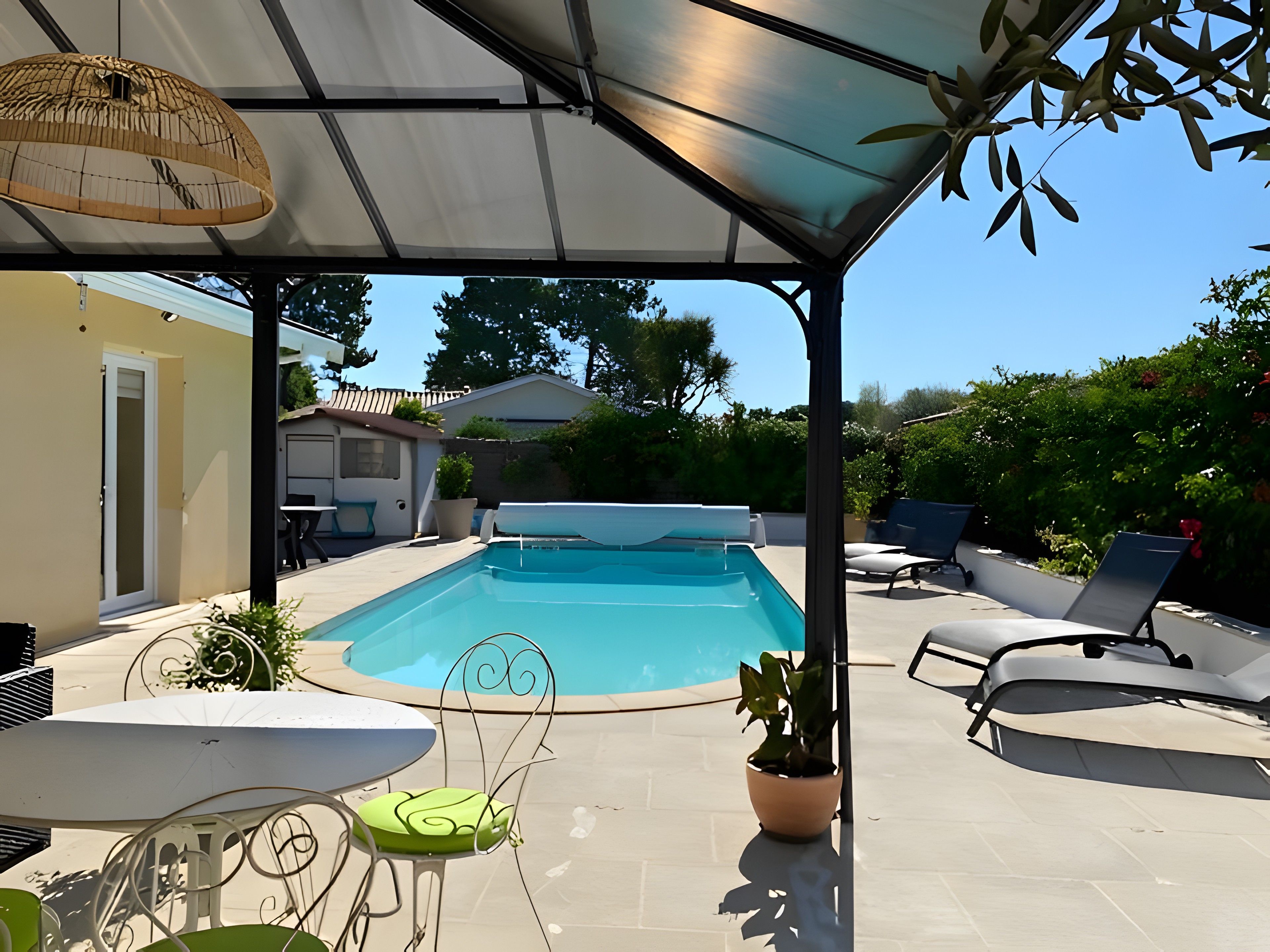 A covered outdoor area with a swimming pool, lounge chairs, and a table with chairs.