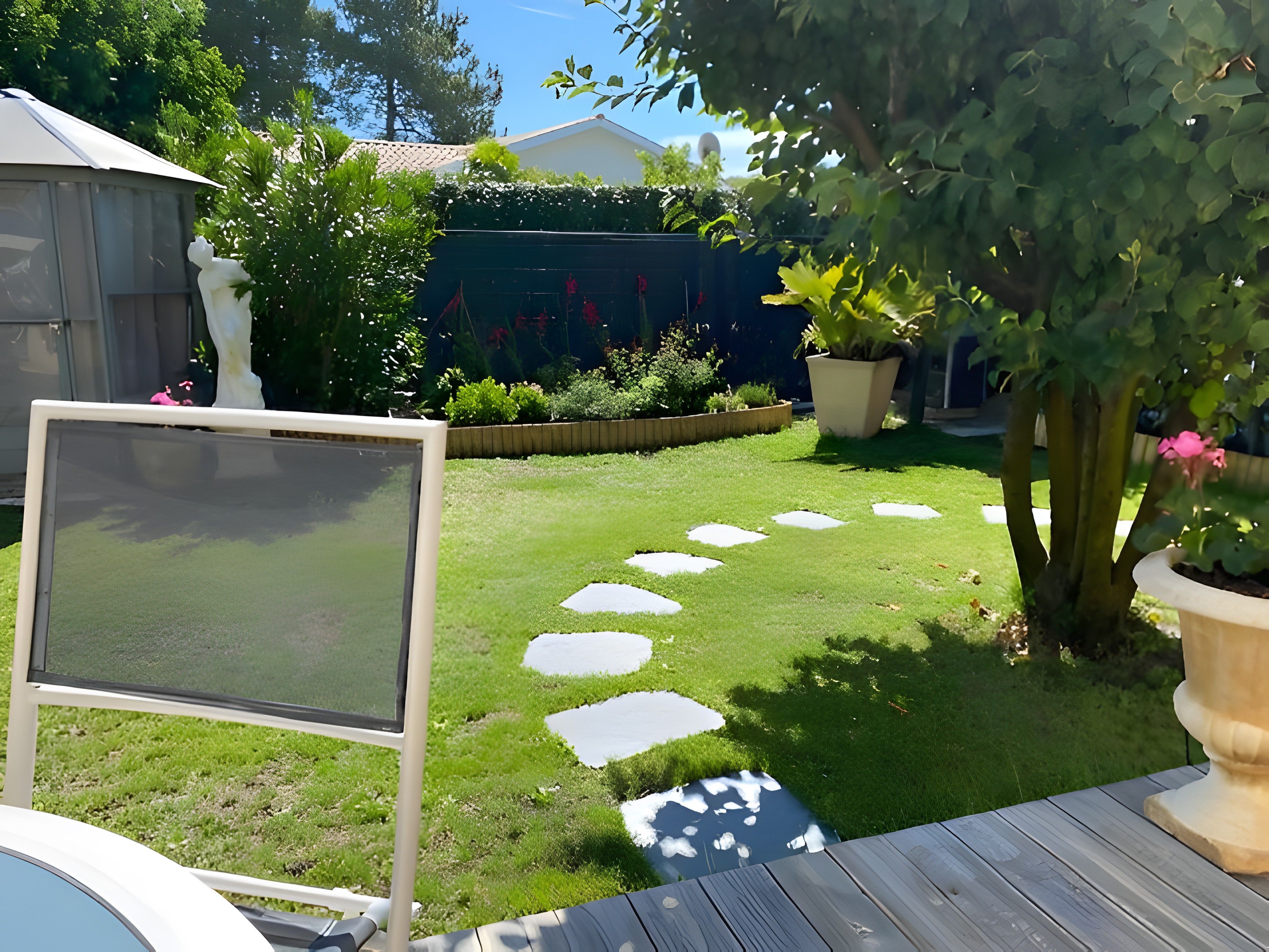 A garden with a paved path, a white screen, and a wooden deck.