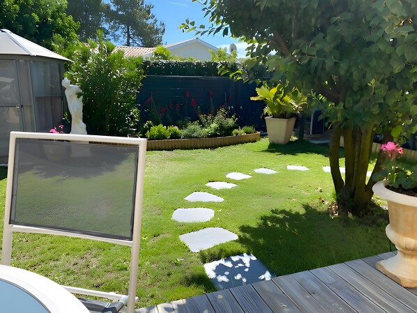 Een tuin met een geplaveid pad, een wit scherm en een houten terras.