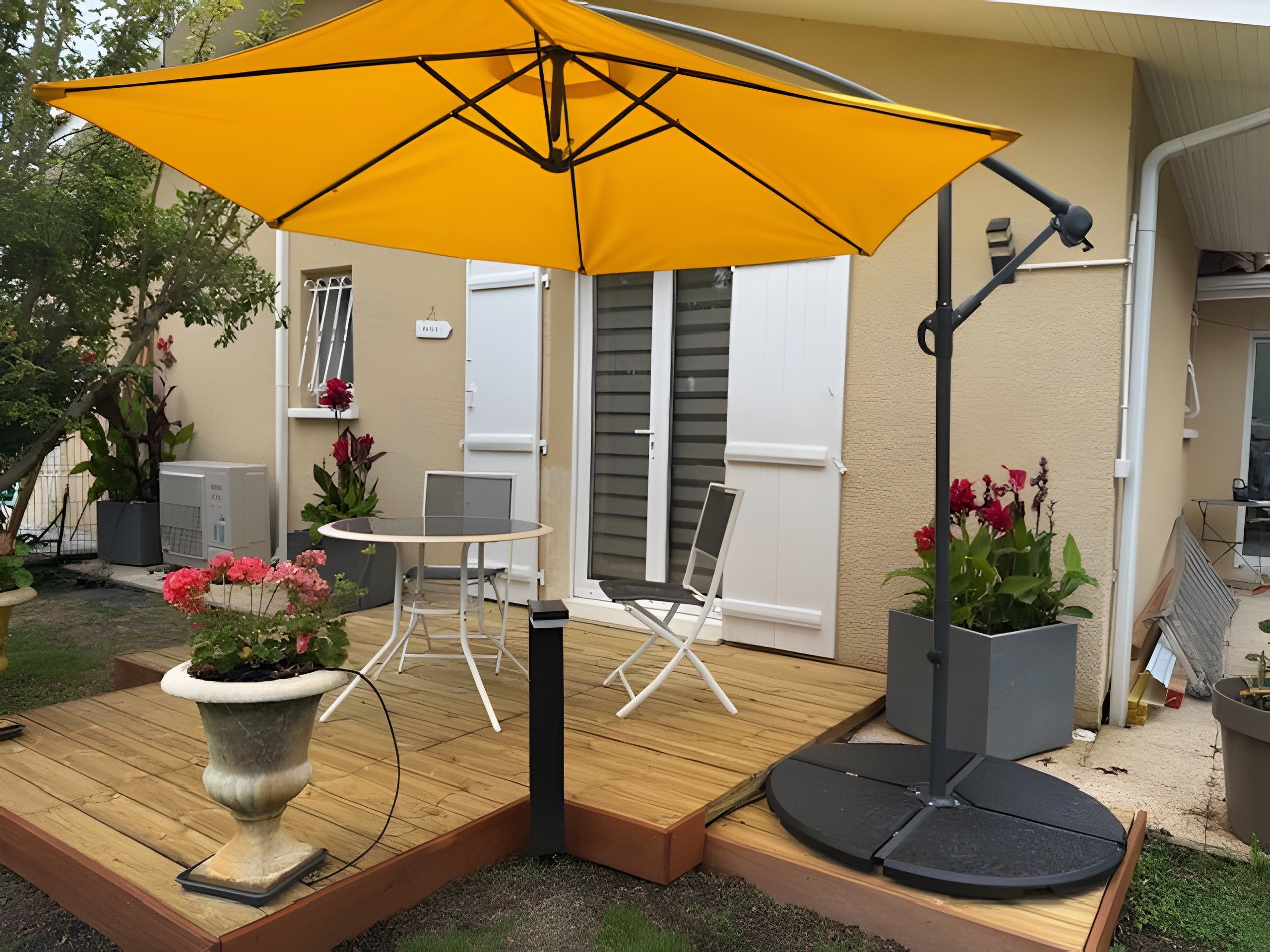 A patio with a yellow umbrella, a table, chairs, and potted plants.