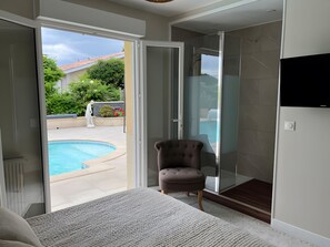 A room with a glass door leading to a swimming pool, a cushioned chair, and a flat-screen TV mounted on the wall. - Guest Room 'Chambre Jeu D'Eau' with Shared Terrace, Wi-Fi and Air Conditioning (Gujan-Mestras)