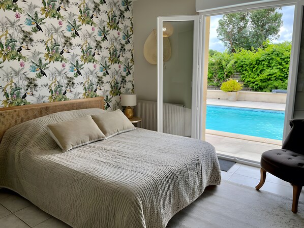 A bedroom with a bed, a nightstand, a lamp, and a view of a swimming pool. - Guest Room 'Chambre Jeu D'Eau' with Shared Terrace, Wi-Fi and Air Conditioning (Gujan-Mestras)