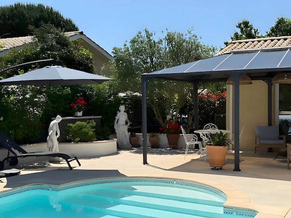 Ein Poolbereich mit einer Pergola, Sitzgelegenheiten im Freien und Statuen.