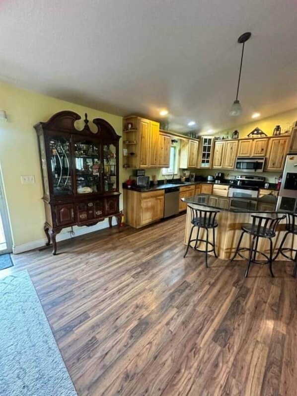 A spacious kitchen with wooden cabinets, a central island with stools, and a traditional wooden dining table. - Wild Outdoor Adventures MT Craig, Flyfishin Suite (Cascade County)