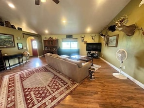 Un salon avec un canapé, un tapis, un ventilateur et des têtes d’animaux empaillées accrochées au mur.