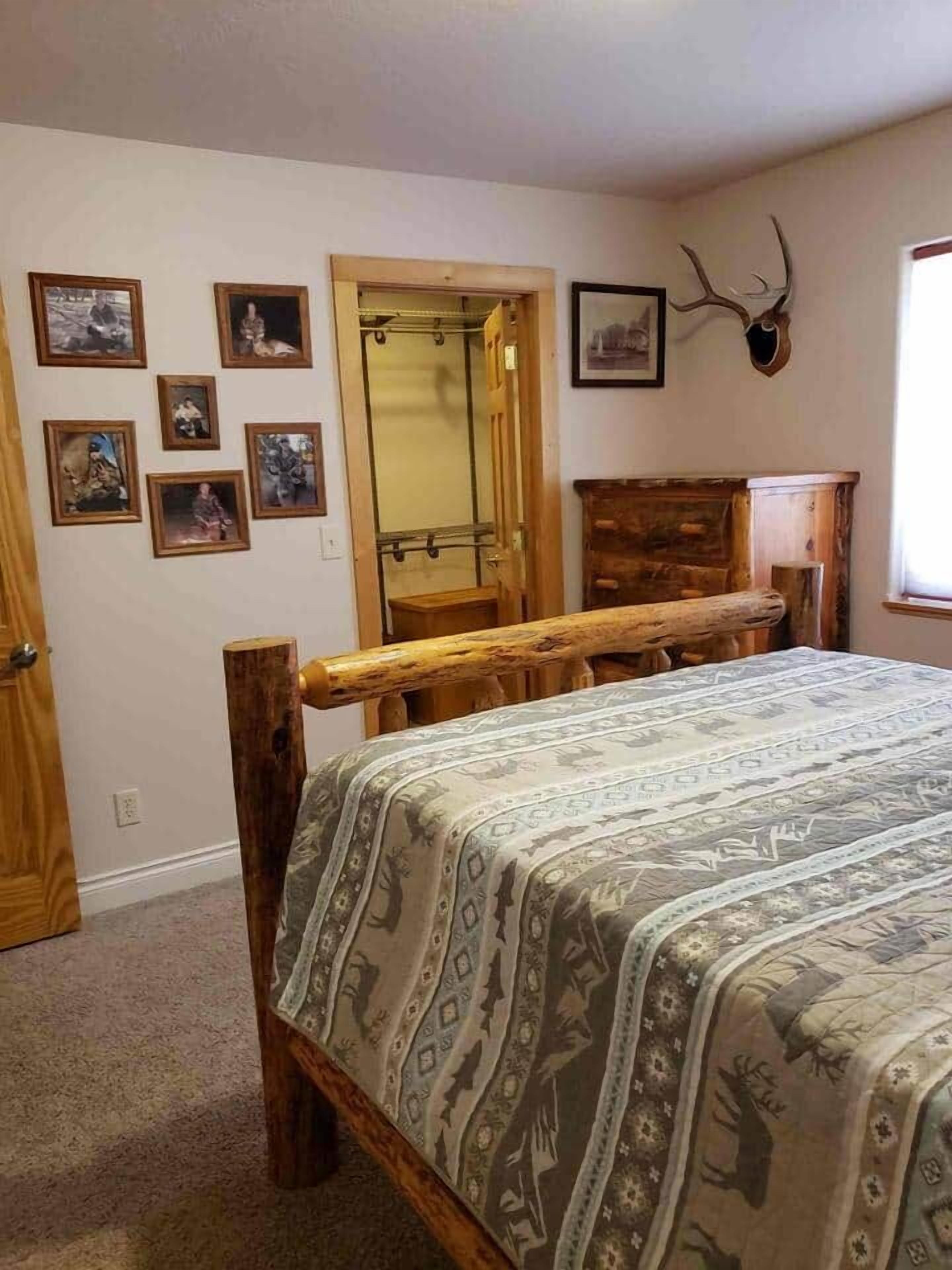 Une chambre à coucher avec un lit en bois, une tête de cerf accrochée au mur et plusieurs tableaux encadrés qui décorent le mur.