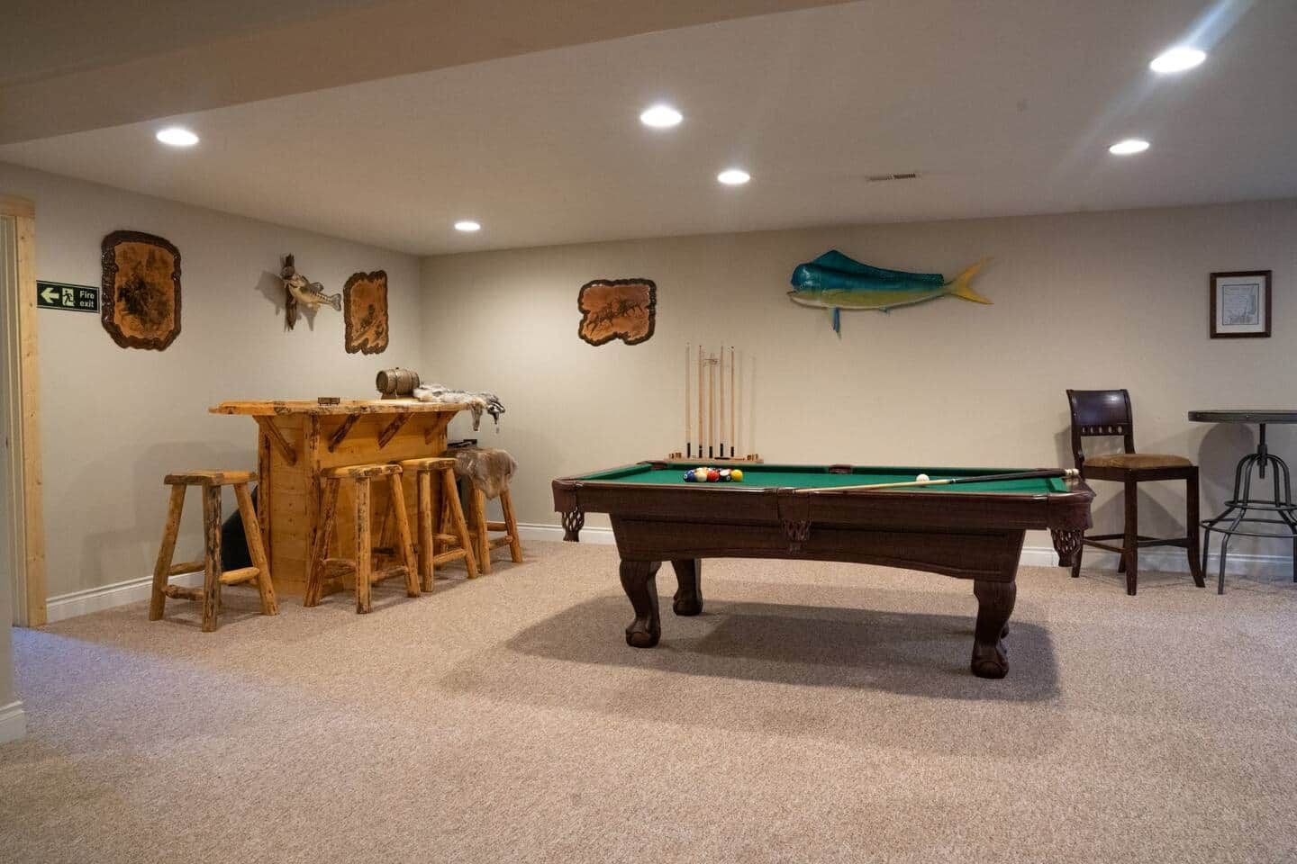 Une table de billard recouverte d’un drap vert, entourée de tabourets en bois et d’un coin bar au design rustique.