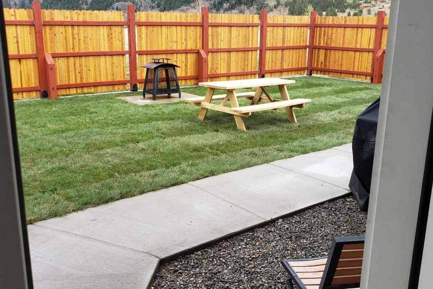 Un jardin avec une clôture en bois, une table de pique-nique et un barbecue.
