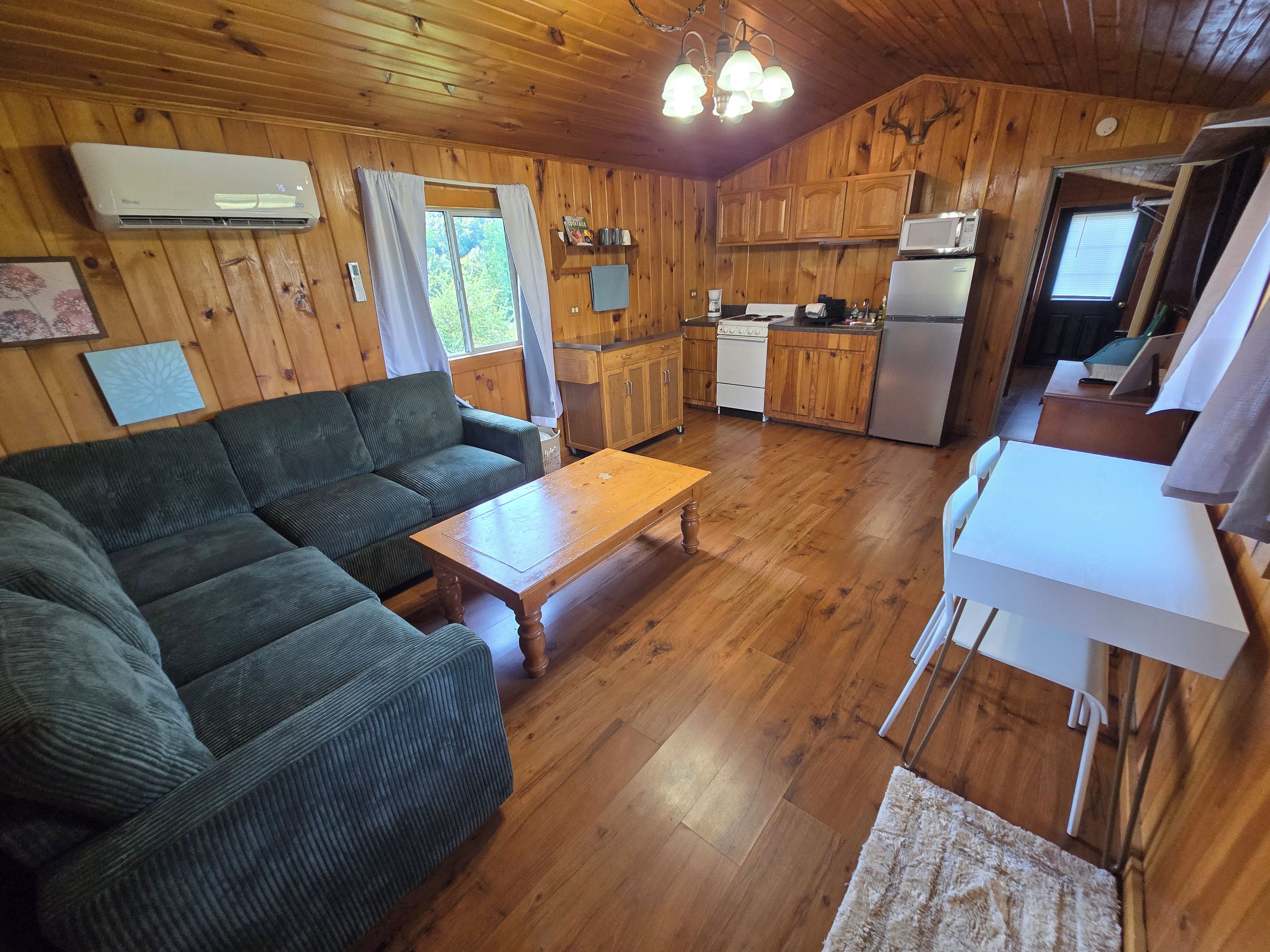 A cabin interior with a sofa, wooden dining table, kitchenette, and a ceiling fan.