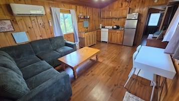 A cabin interior with a sofa, wooden dining table, kitchenette, and a ceiling fan.