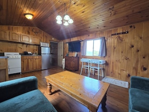 Een houten chalet van binnen, met een keuken, eethoek en een raam met gordijnen.