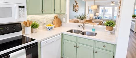 A kitchen with a microwave, stove, sink, and green cabinets.