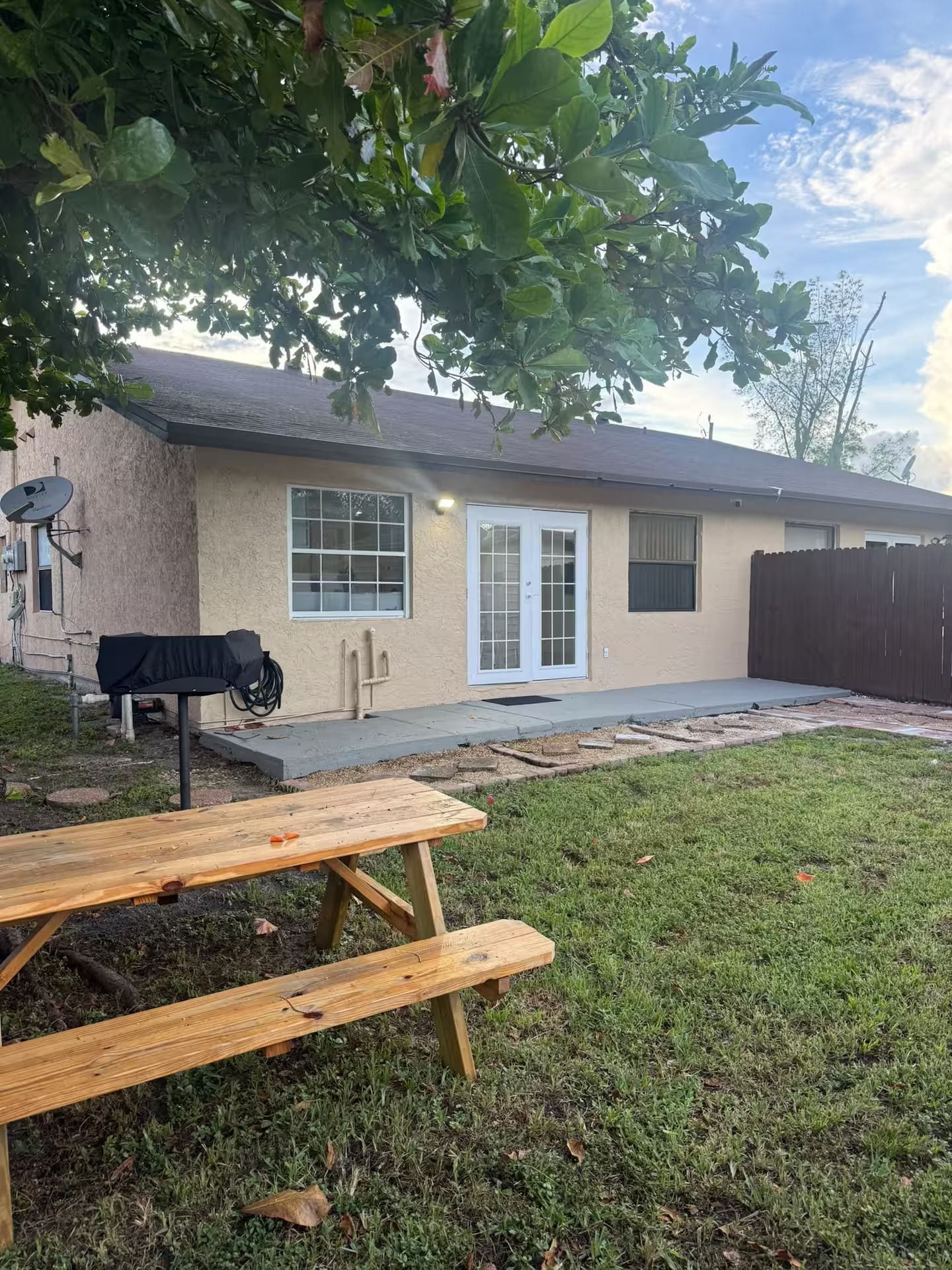 A residential house with a patio, a barbecue grill, and a wooden picnic table.