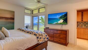 A bedroom with a bed, a TV, a ceiling fan, and a view of the ocean.