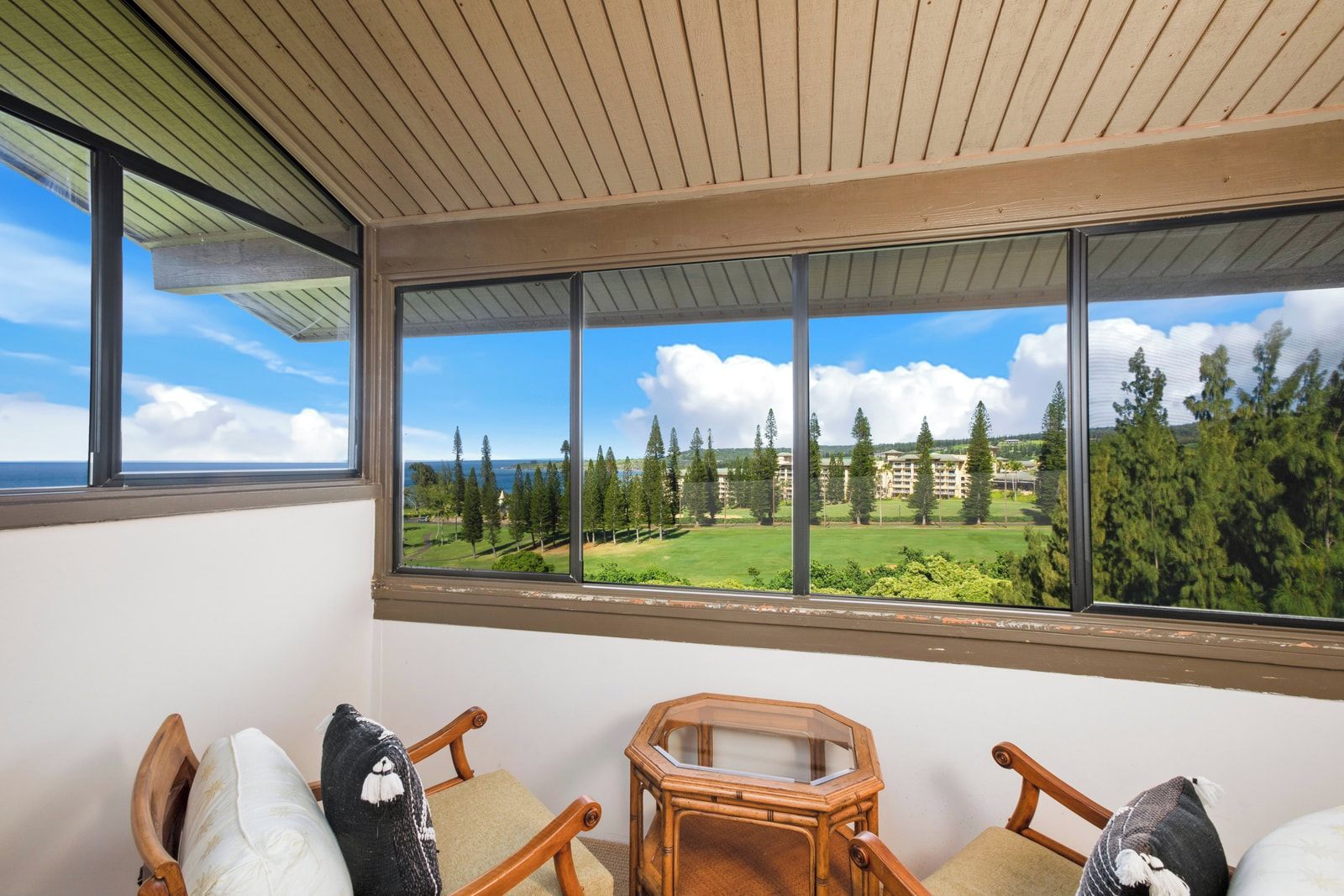 A room with a large window, wooden ceiling, and a view of a golf course and buildings.