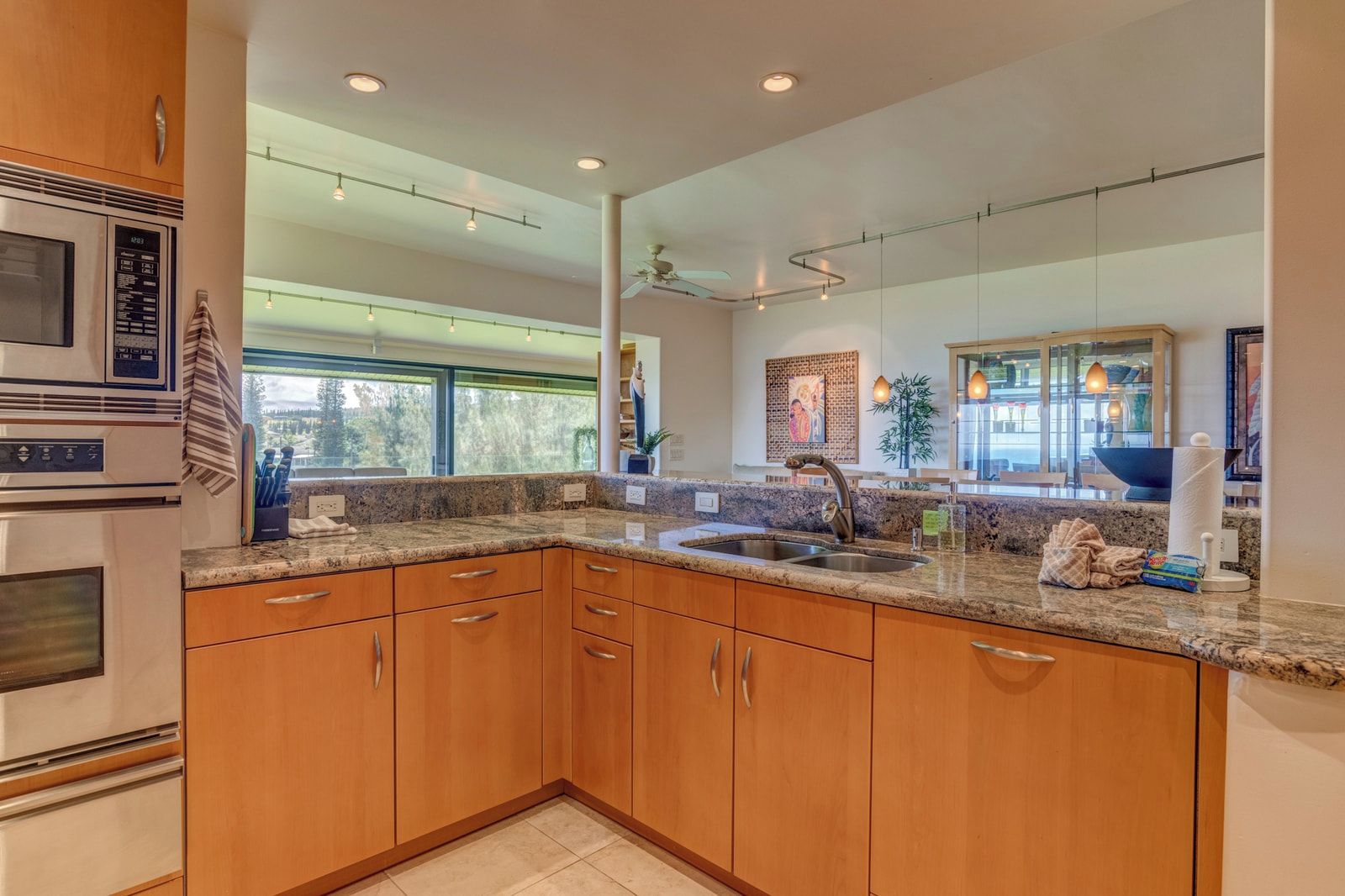 A modern kitchen with granite countertops, wooden cabinets, a stainless steel sink, and a built-in oven.
