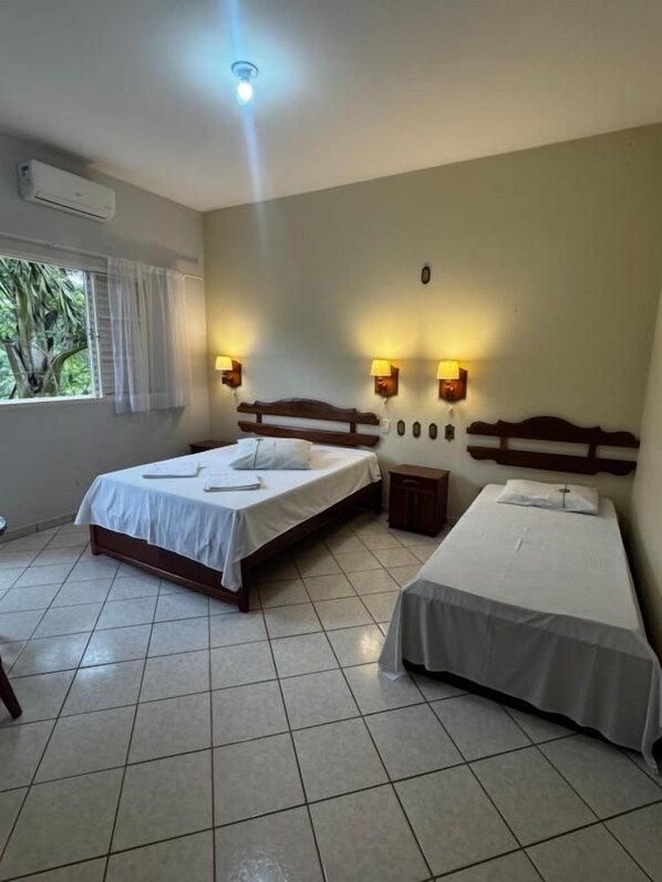 A room with two beds, a window with curtains, and wall-mounted lights.