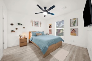 Un dormitorio con cama, mesitas de noche, ventilador de techo y obras de arte en las paredes.