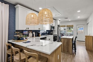 Una cocina moderna con armarios blancos, encimera de mármol y una isla central con asientos.