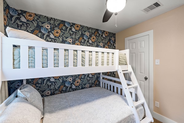 Una cama litera con escalera, una puerta y un ventilador de techo en una habitación con papel tapiz floral.