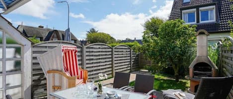An outdoor patio with a table set for dining, surrounded by chairs, a barbecue grill, and a wooden fence.