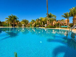Una piscina de blau clar envoltada de palmeres i un edifici amb cúpula.