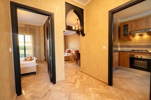 Habitació d'hotel amb llit, zona de menjador amb sofà i cuina amb armaris de fusta i fogó.