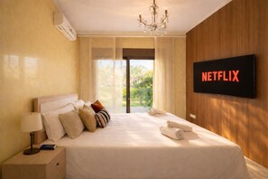 Ein Hotelzimmer mit einem Bett, einem Fernseher, der 'NETFLIX' anzeigt, einem Nachttisch mit einer Lampe und Blick auf Grünfläche.