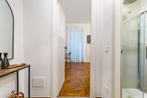 En hall med trägolv, en vit vägg, en dörr med ett glasparti och en vit gardin.
