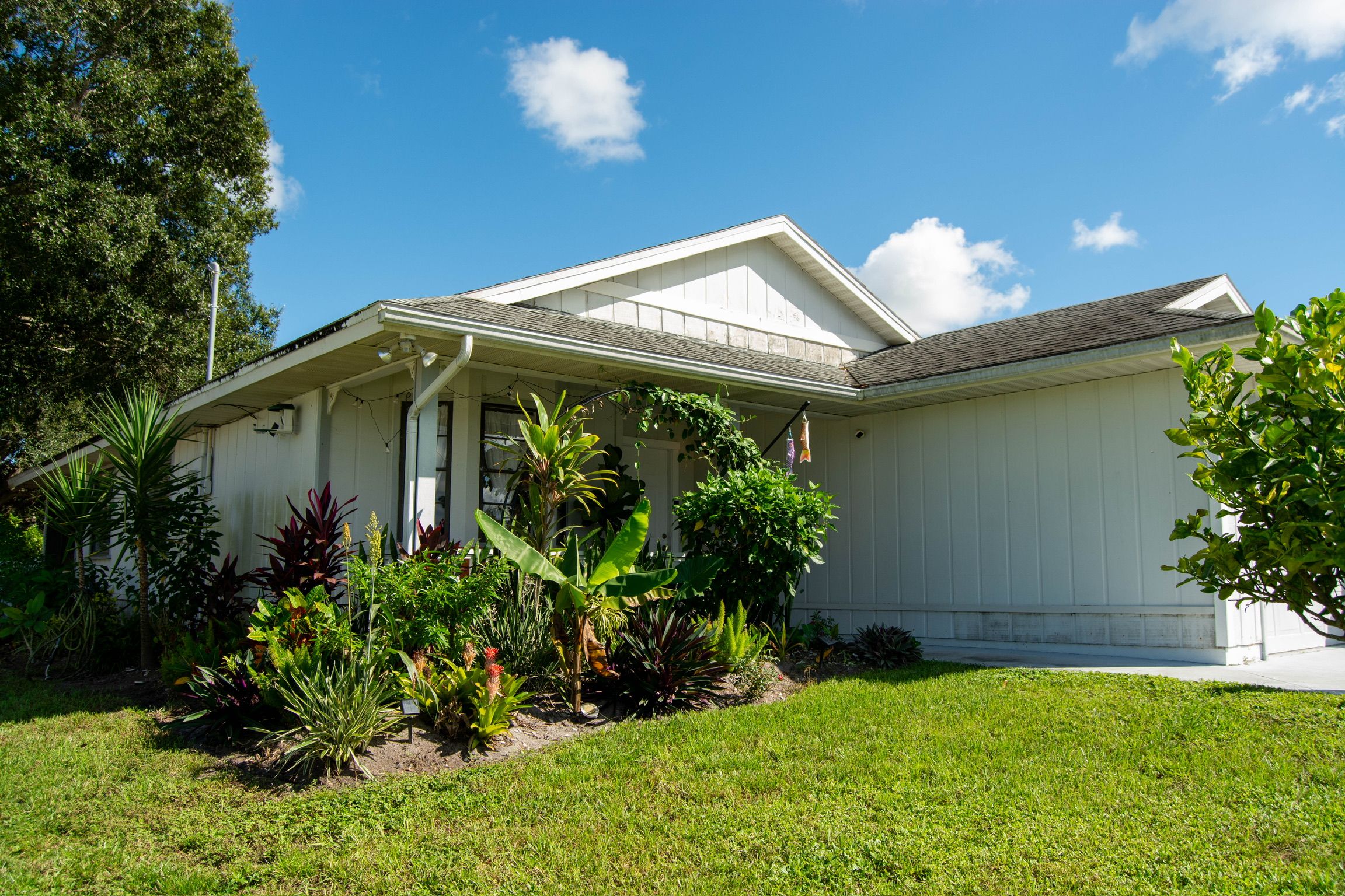 A single-story house with a covered porch, surrounded by a well-maintained lawn and various tropical plants.