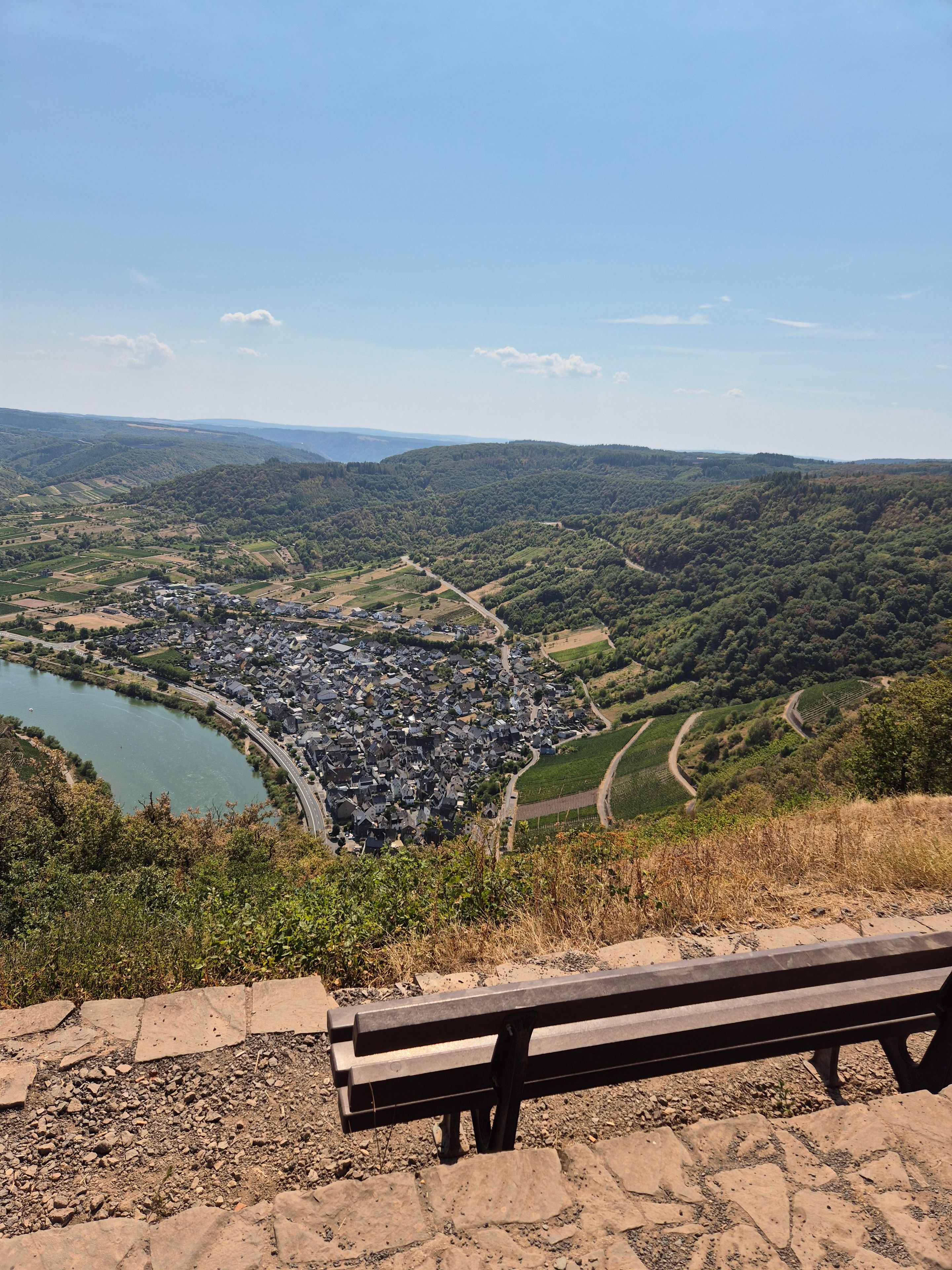 Eine Bank mit Blick auf eine Stadt und einen Fluss, umgeben von Hügeln.