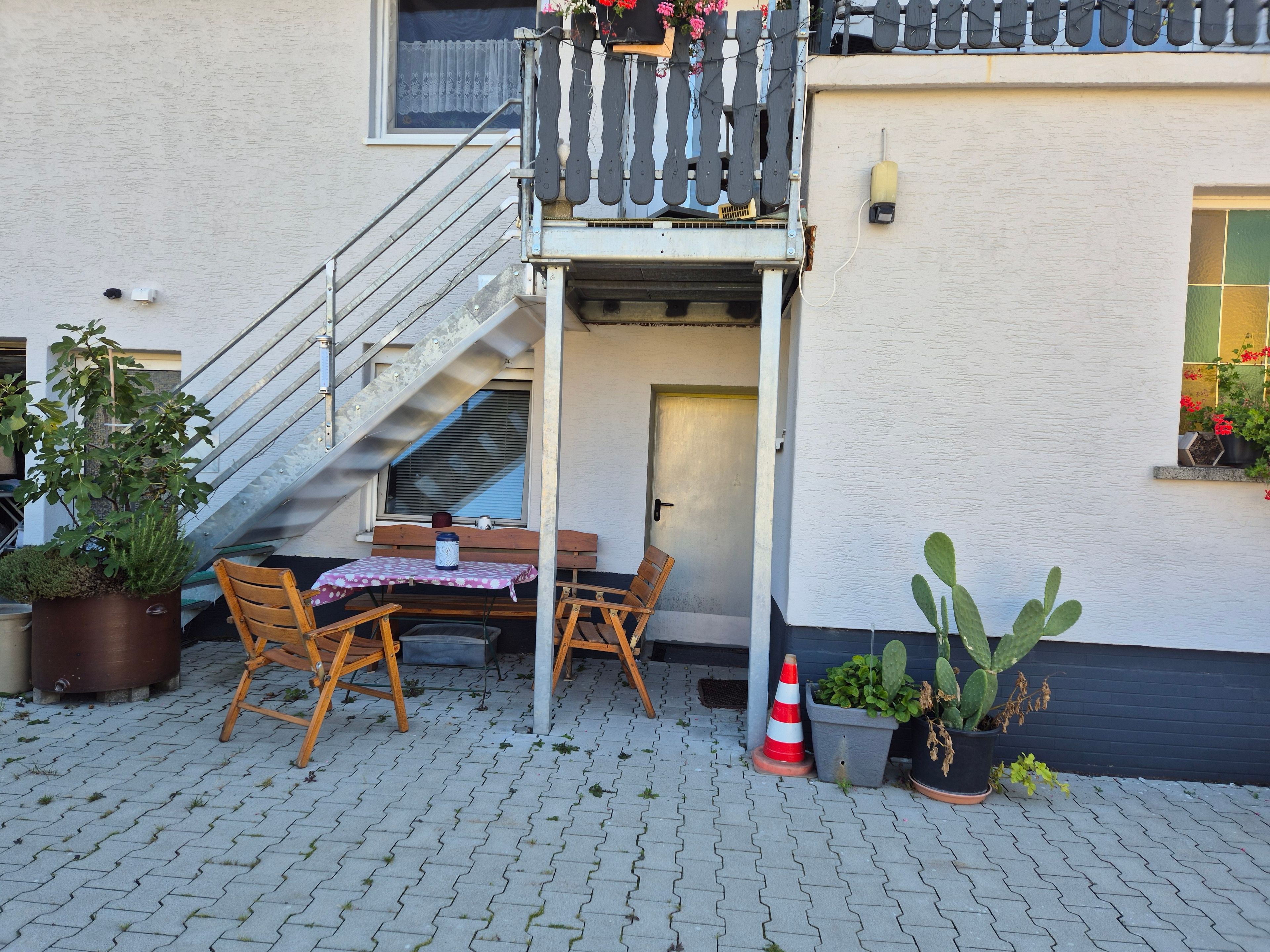 Eine Terrasse mit Tisch, Stühlen, einem Blumentopf, einer kleinen Treppe und einer Tür.