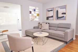 A modern living room with a grey sofa, a round coffee table, and a chair. There are abstract paintings on the wall and a built-in shelf unit. - Home with gorgeous backyard and pool in Fort Lauderdale (Fort Lauderdale)