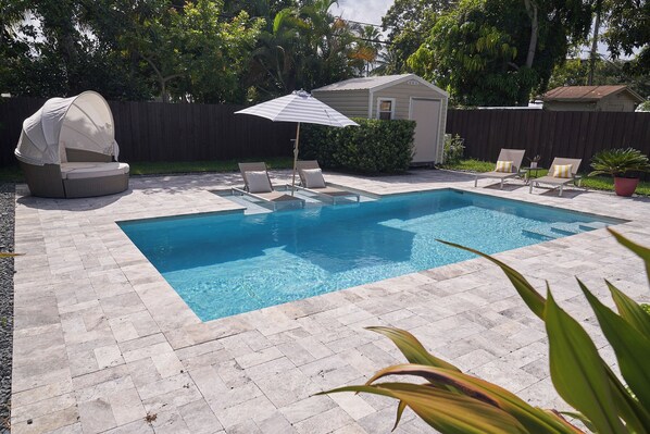 A rectangular swimming pool with a tiled deck, surrounded by lounge chairs and a covered seating area. - Home with gorgeous backyard and pool in Fort Lauderdale (Fort Lauderdale)