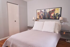 Une chambre à coucher avec un lit, une porte, un tableau accroché au mur et des lampes de chevet.