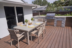 Une terrasse extérieure avec une table à manger, des chaises et un barbecue.