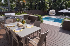 Une terrasse extérieure avec une table à manger, des chaises, un barbecue et un espace piscine.