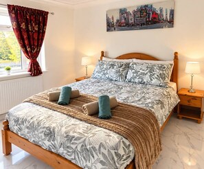 Un letto rifatto con cura, una coperta a fiori, due cuscini e una coperta in tessuto intrecciato.