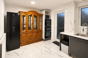 Una cucina con frigorifero nero, pensili in legno, forno integrato e zoccolo in marmo.