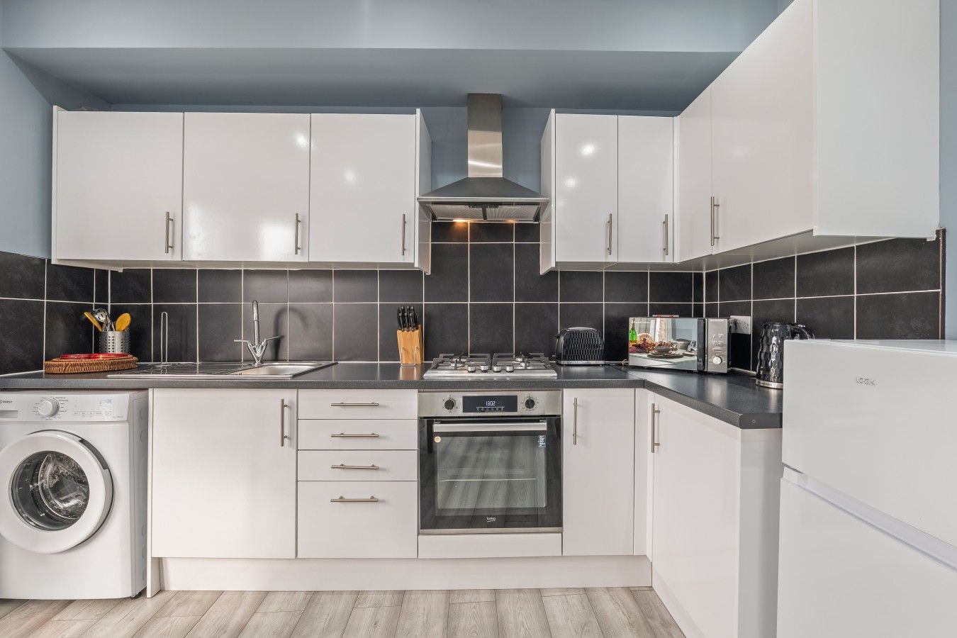 A modern kitchen with white cabinets, a stainless steel range, a built-in oven, and a washing machine.